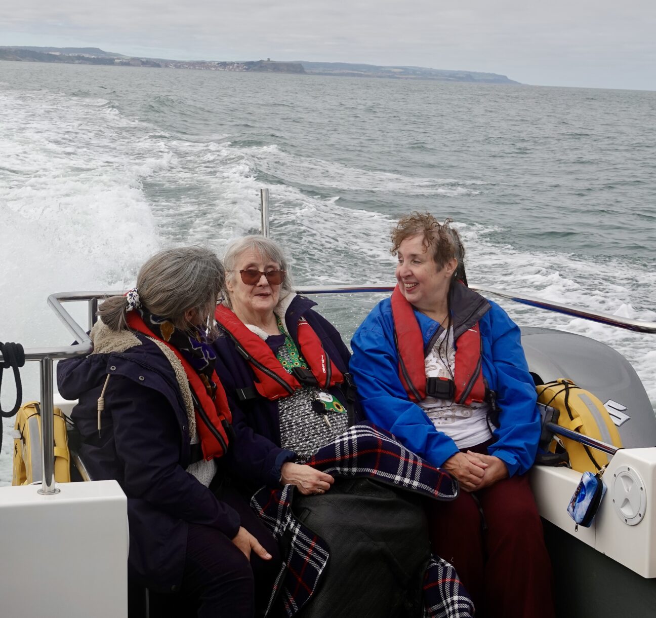 Three womensit wearing buoyancy aids at the back of the boat, chatting and looking for wildlife.