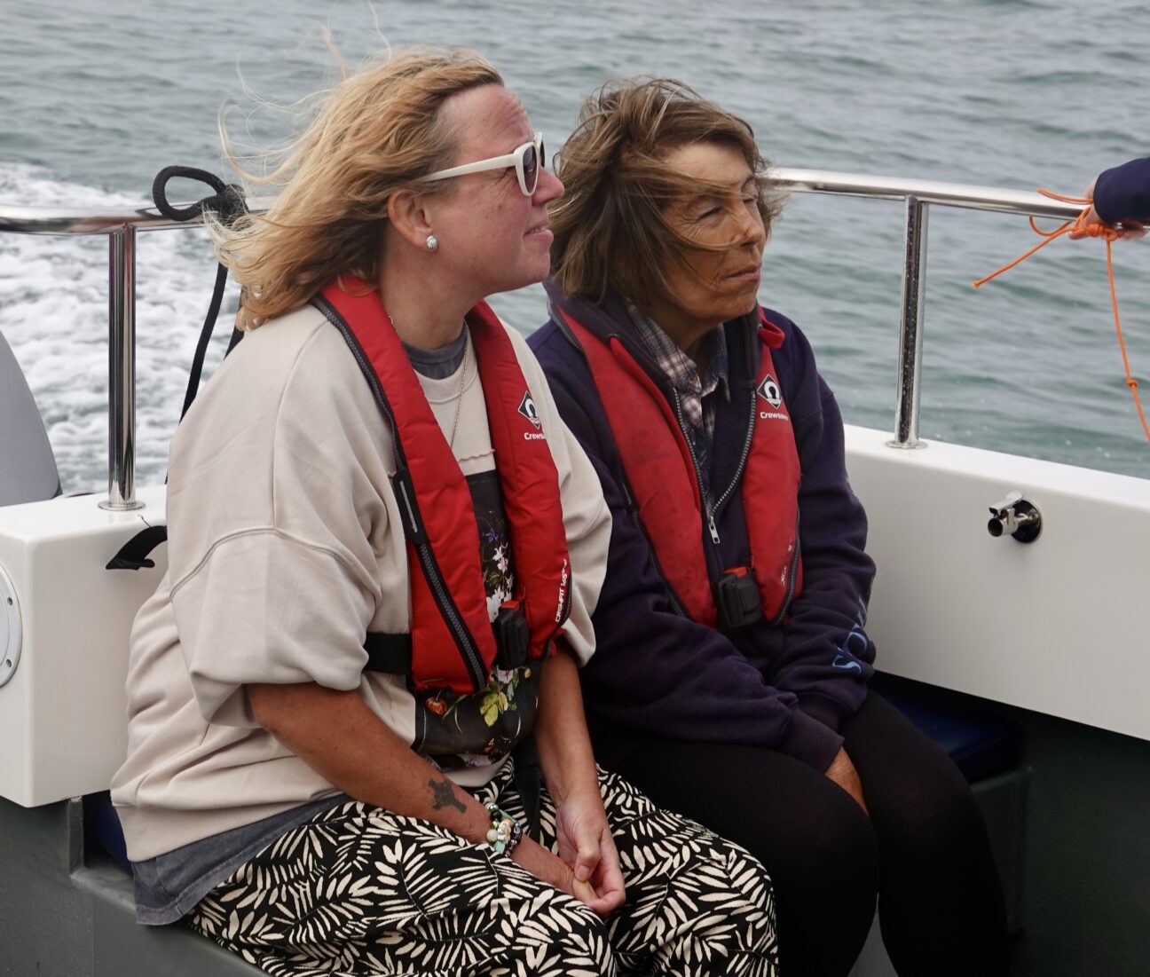 Two ladies sit wearing buoyancy aids at the back of the boar, looking for marine wildlife.