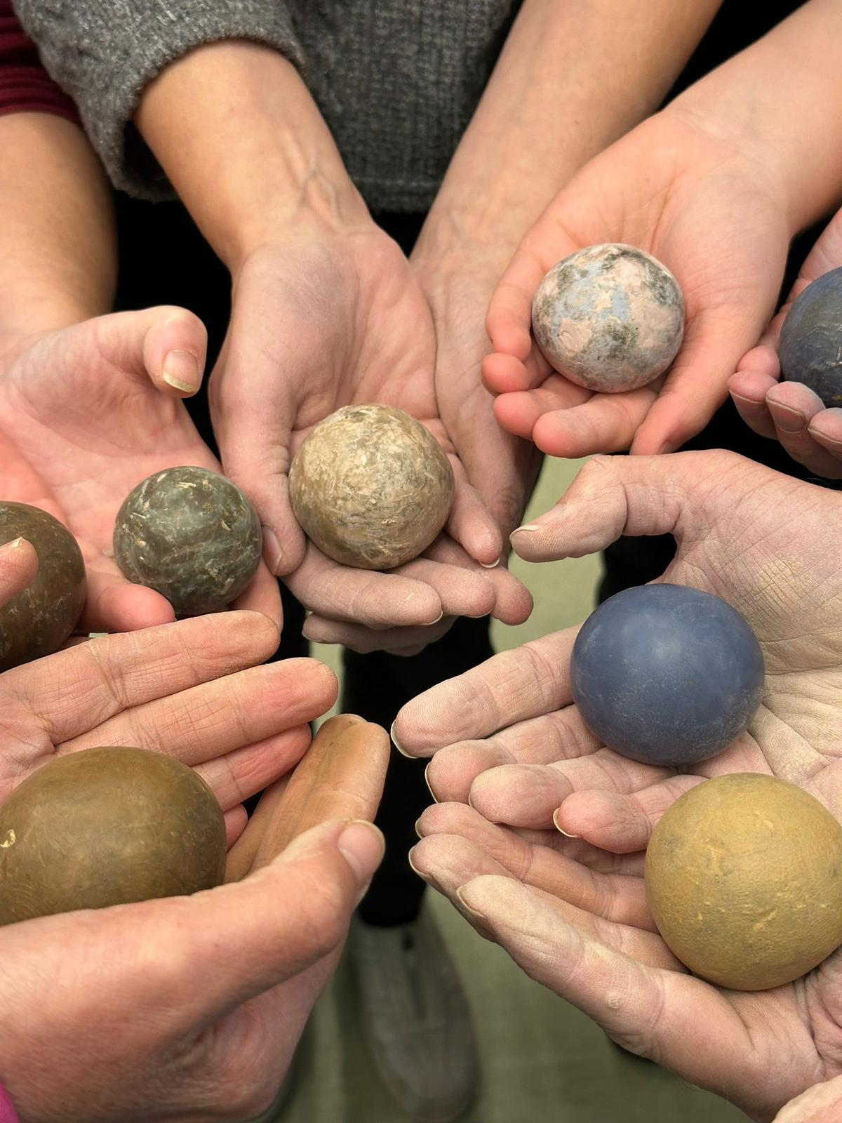 Hands holding Dorodango balls of different sizes and colours made