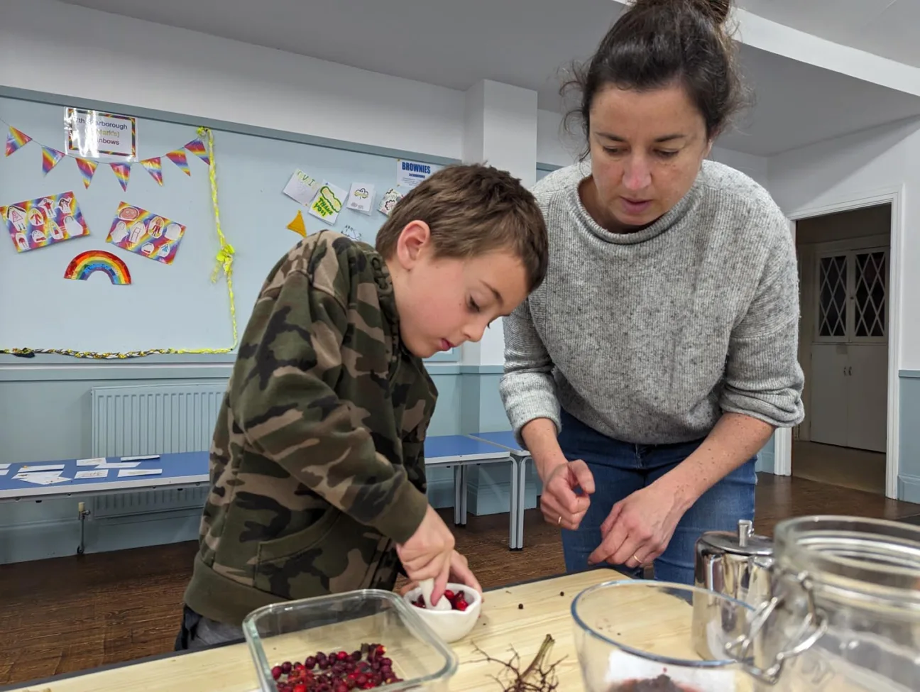 Artist Emma Smith leans over to help a young boy crush berries with a pestle and mortar