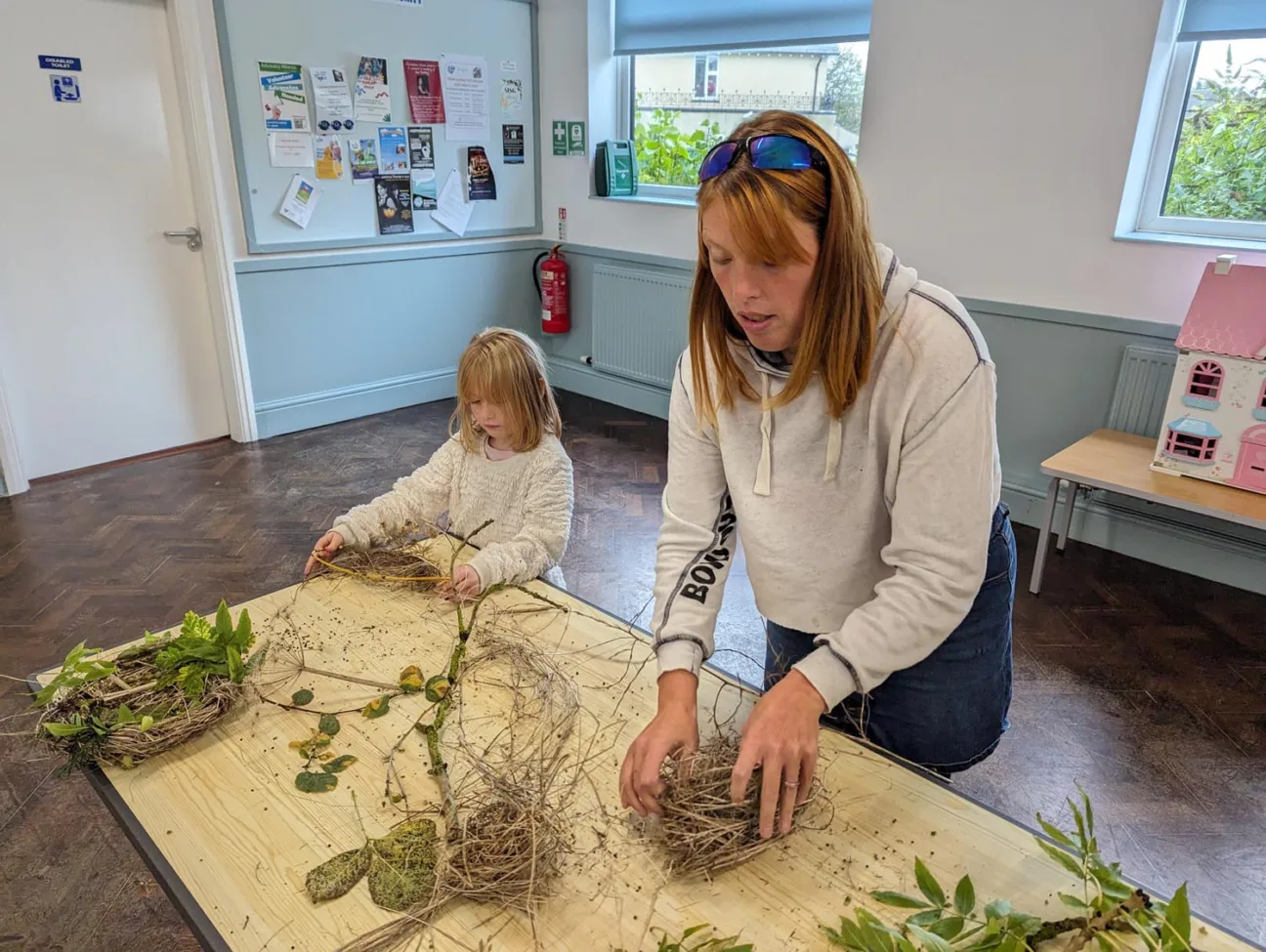 A parent and child create habitats for wildlife using natural materials, including sticks and leaves, found along the Cinder Track