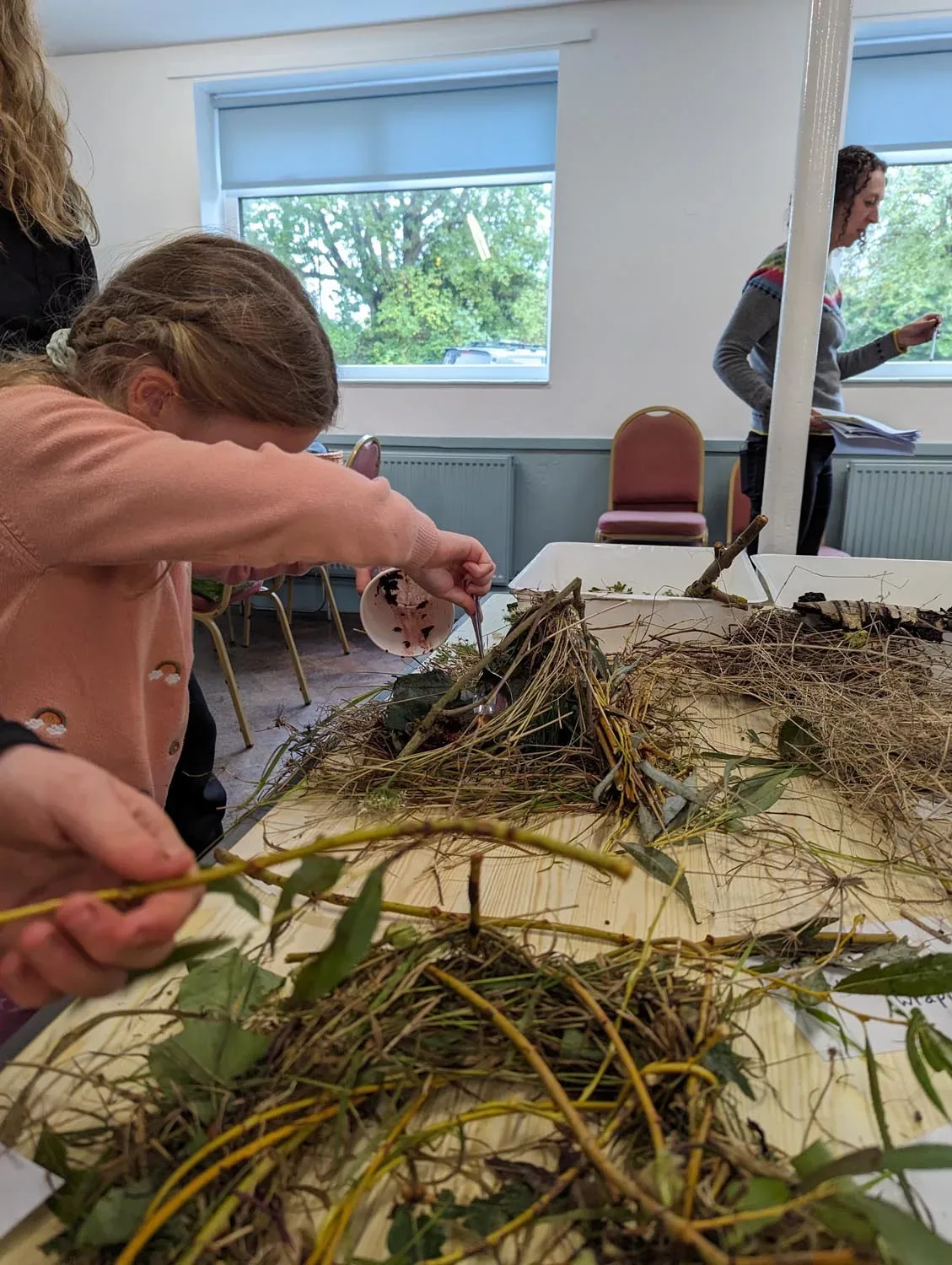 A child stands next to a table, where they carefully place sticks in a pyramid shape to create a habitat for wildlife