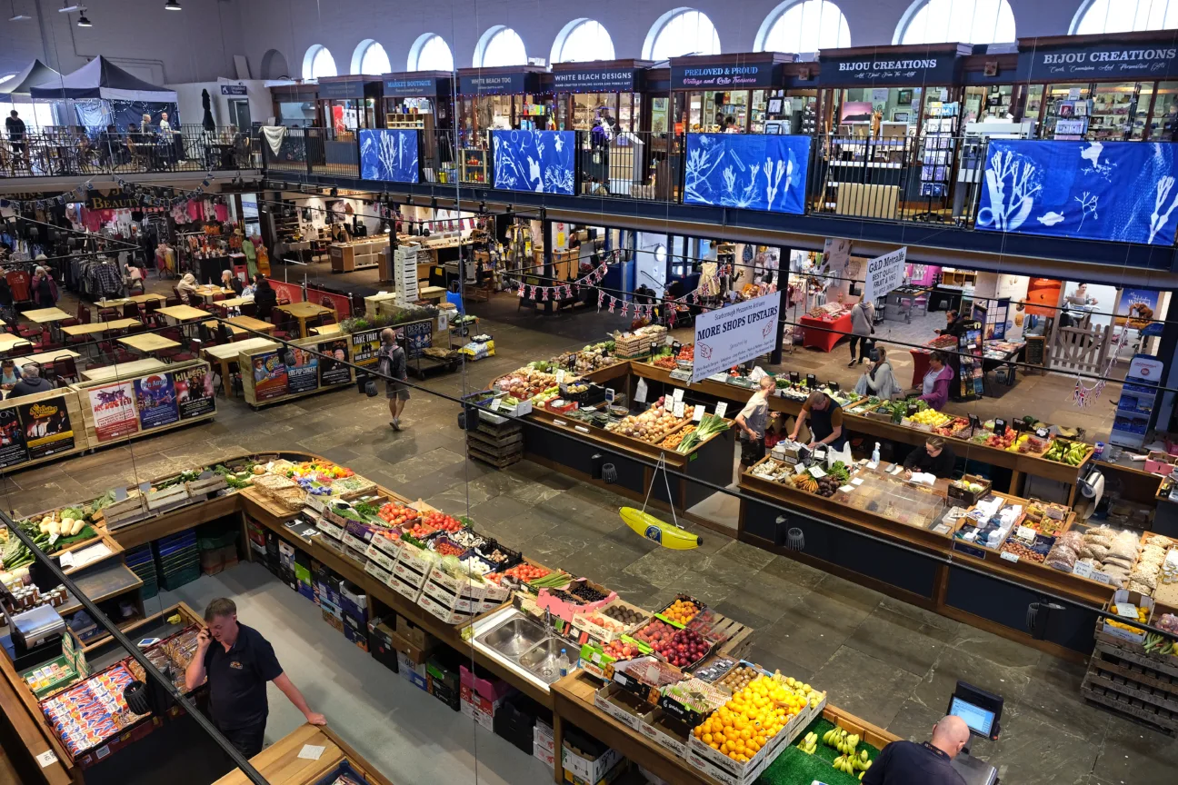 Large blue and white banners displayed around Scarborough Market Hall. They are attached to railings high above the market sellers.