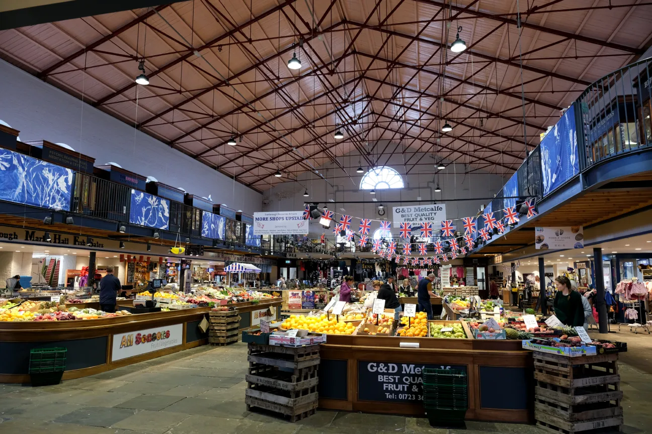 Large blue and white banners displayed around Scarborough Market Hall. They are attached to railings high above the market sellers.