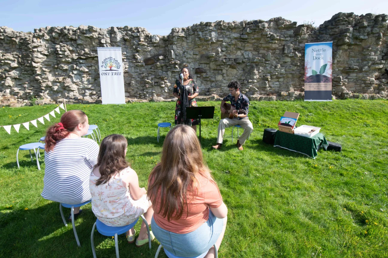 Nettle and Dock, a two person performance group sing and play guitar to a group of onlookers