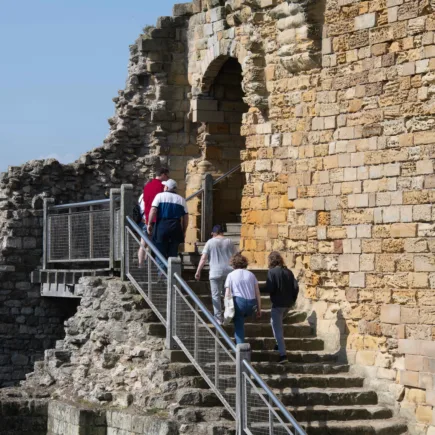 A group of visitors climb the stairs up the side of Scarborough Castle on a sunny day